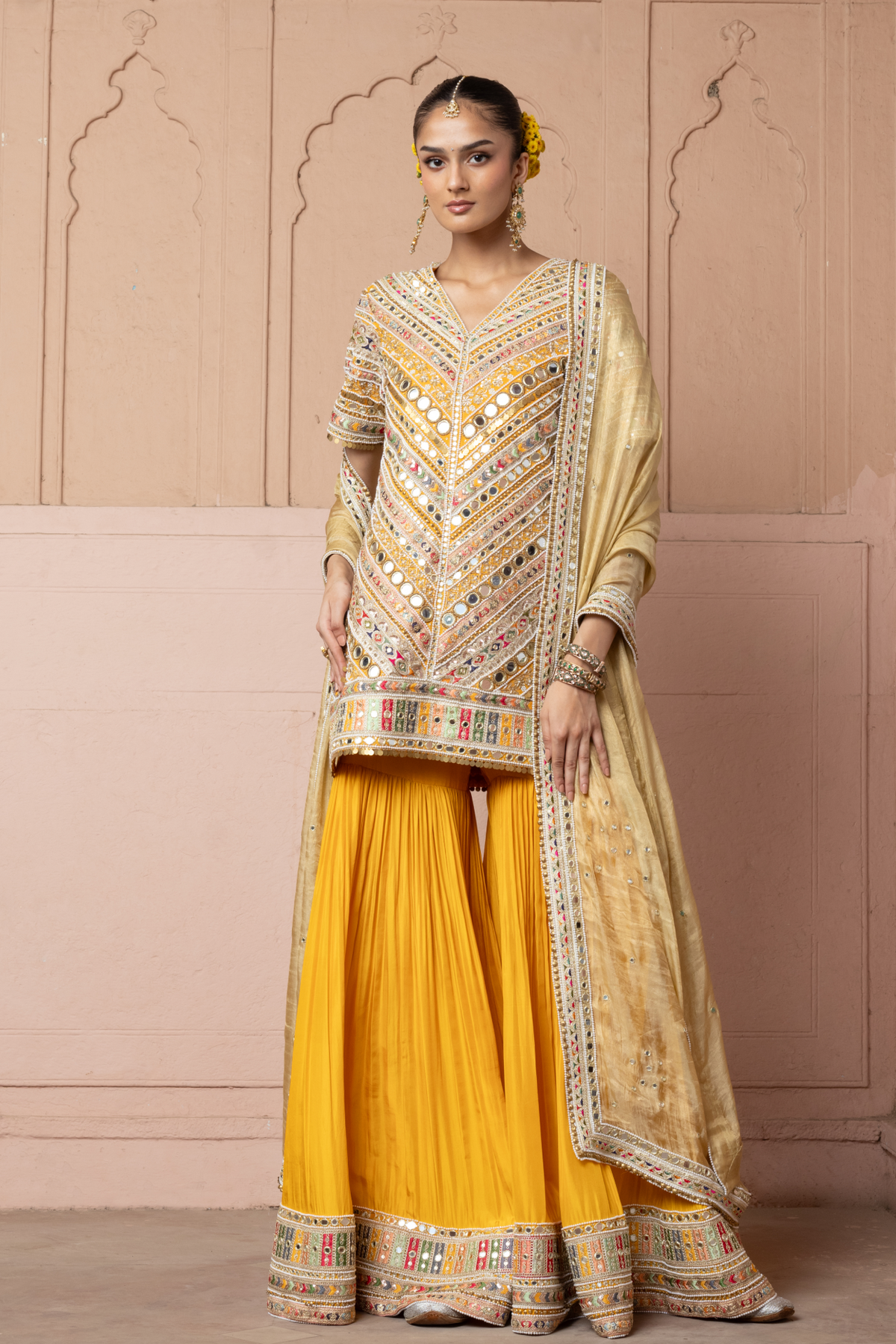 Mustard yellow embroidered kurta with mirror and threadwork detailing, paired with a coordinating flared sharara and gold dupatta.