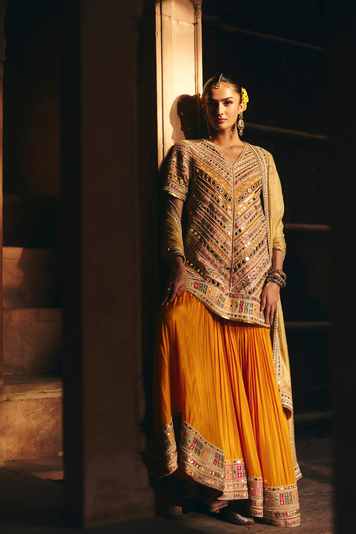 Mustard yellow embroidered kurta with mirror and threadwork detailing, paired with a coordinating flared sharara and gold dupatta.