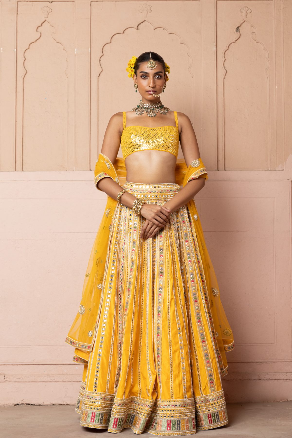 Mustard yellow lehenga adorned with multicolour mirror embroidery, paired with a matching embroidered blouse and sheer embellished dupatta.