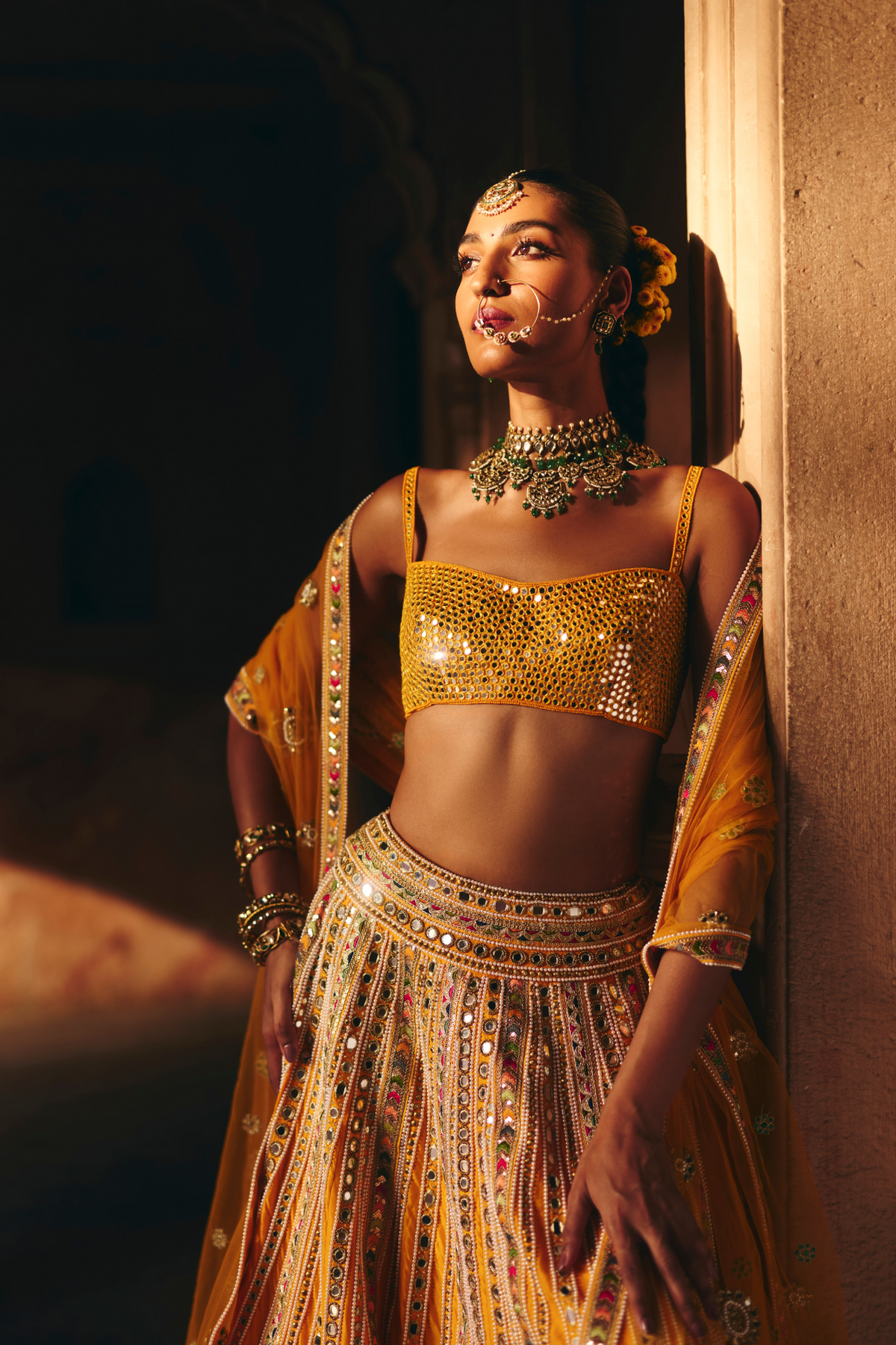 Mustard yellow lehenga adorned with multicolour mirror embroidery, paired with a matching embroidered blouse and sheer embellished dupatta.