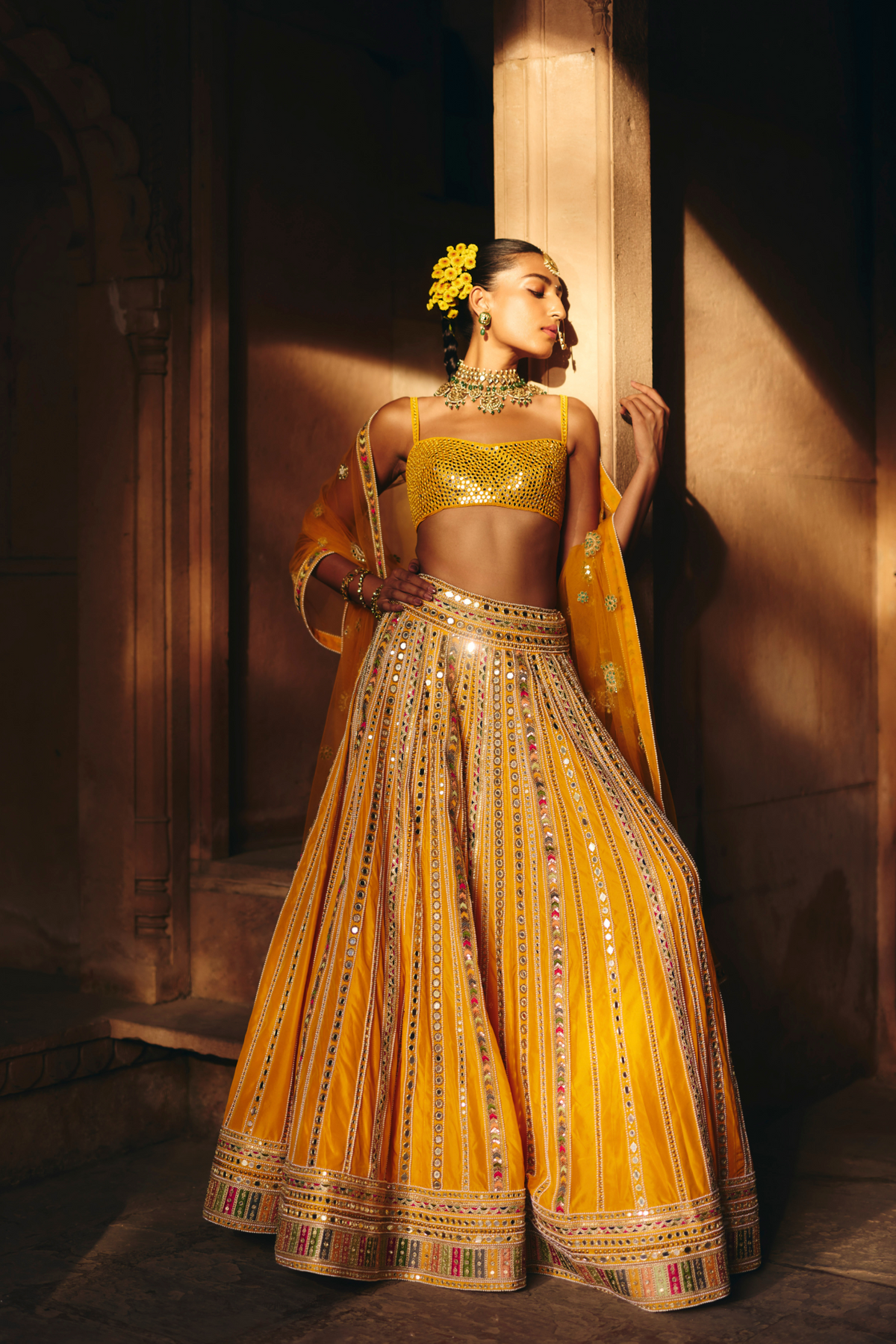 Mustard yellow lehenga adorned with multicolour mirror embroidery, paired with a matching embroidered blouse and sheer embellished dupatta.