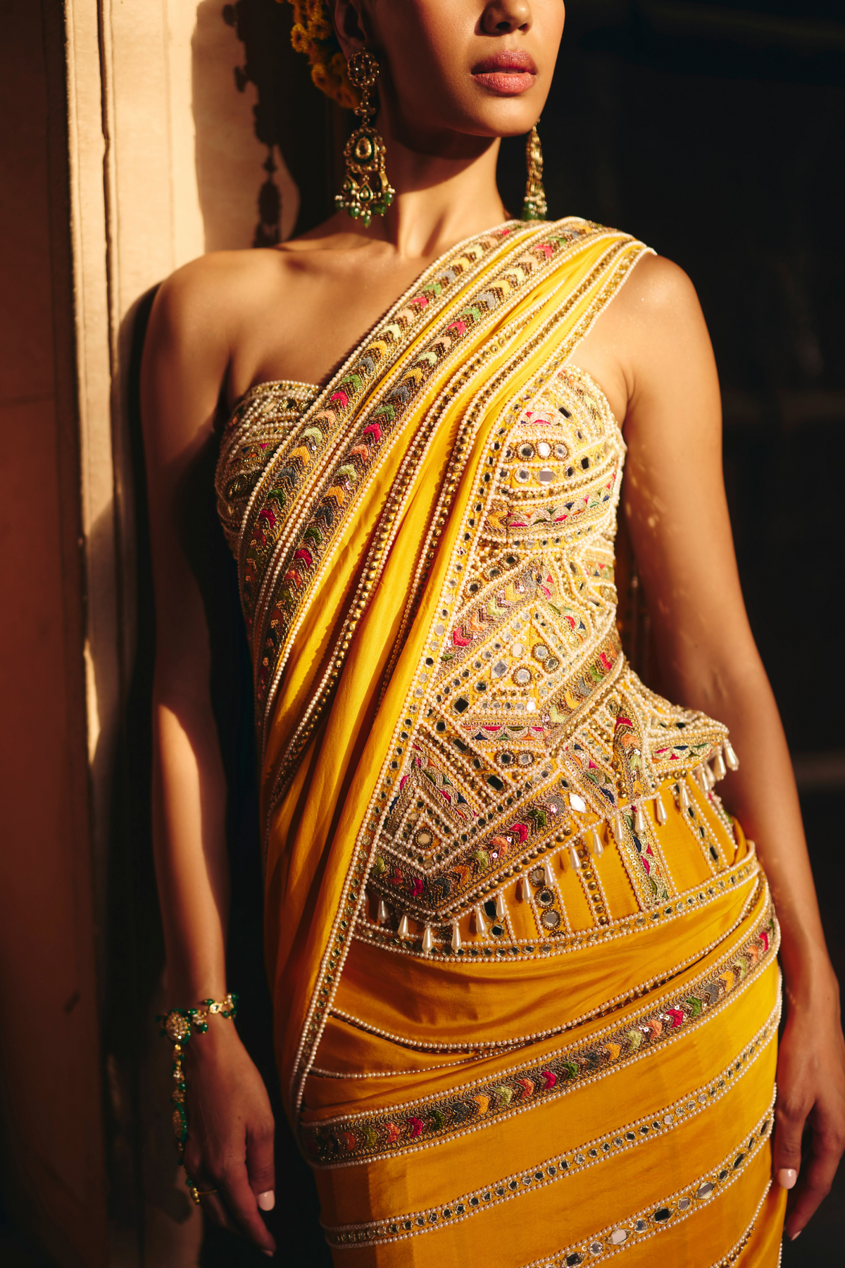Mustard yellow pre-draped saree, paired with a heavily embroidered corset blouse with mirror and sequin embellishments.