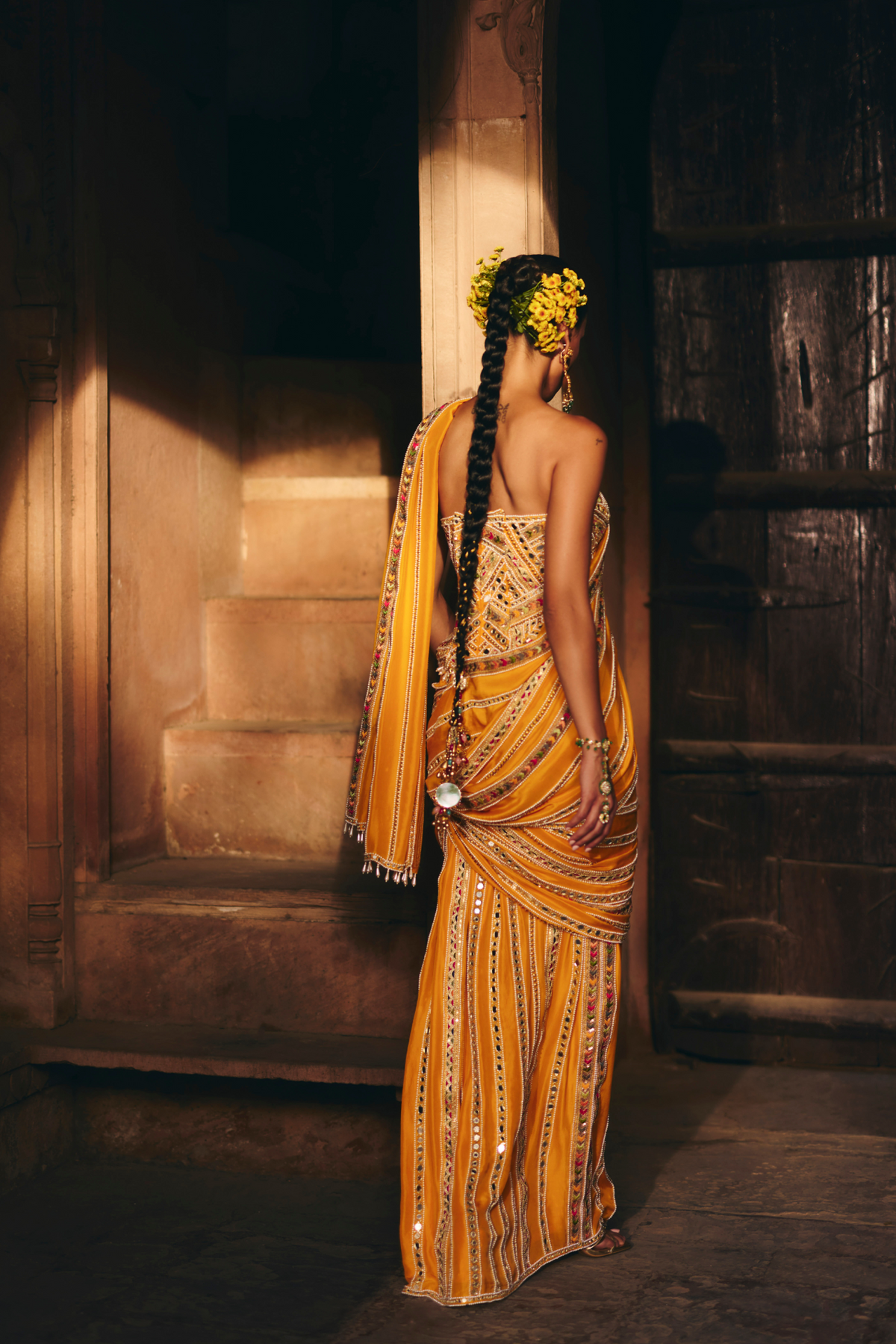 Mustard yellow pre-draped saree, paired with a heavily embroidered corset blouse with mirror and sequin embellishments.
