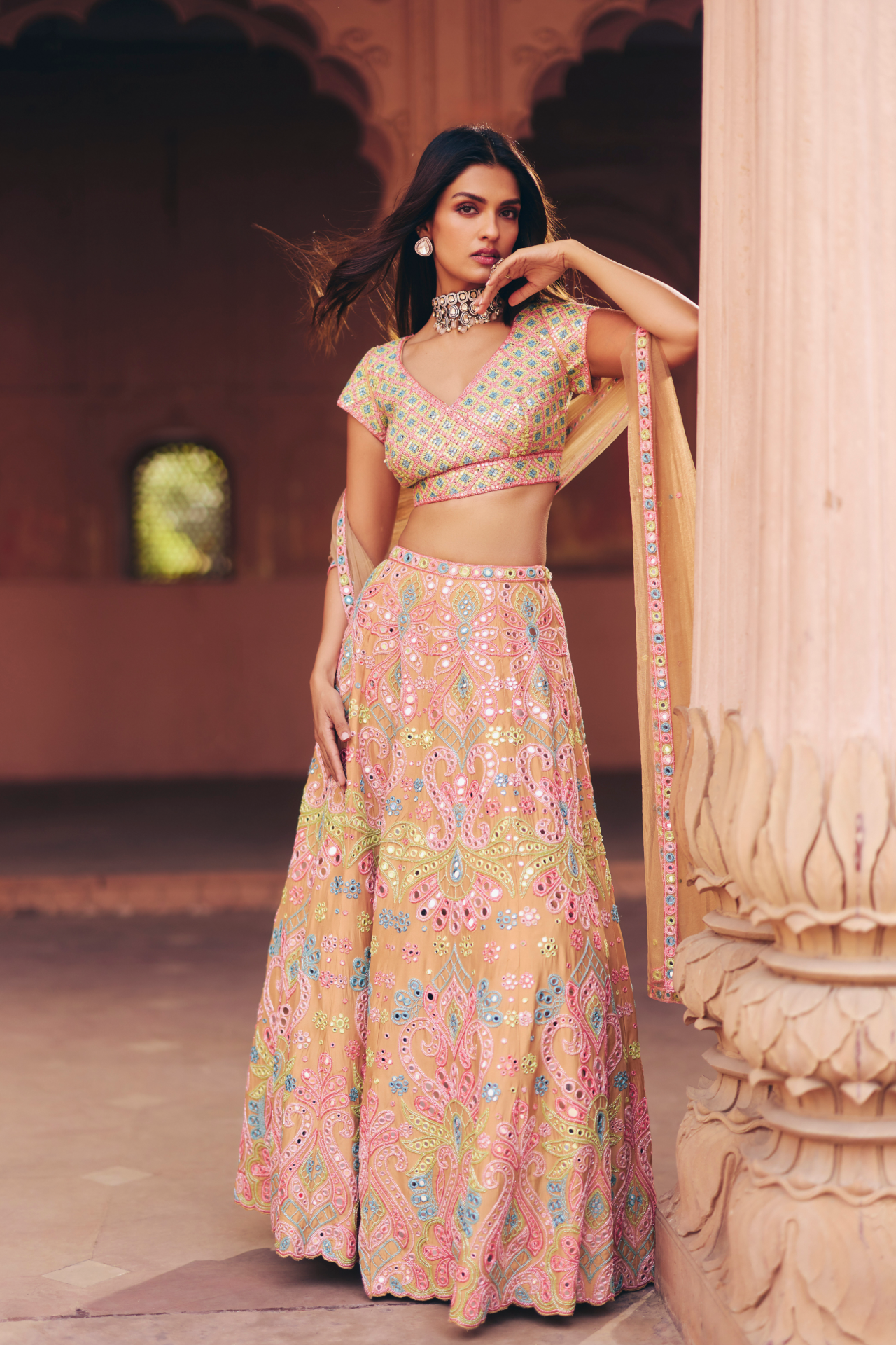 Nude overlap blouse with multicolour mirror embroidery, paired with a flared lehenga and matching net dupatta